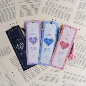 Four bookmarks sitting on a background of torn out book pages. Each bookmark have the same graphic design of a text "Wait a minute", "how f*cking" (in a heart), "far is that, big is that, near is that". Coloured bookmarks from left to right: black, lavender, blue, pink.