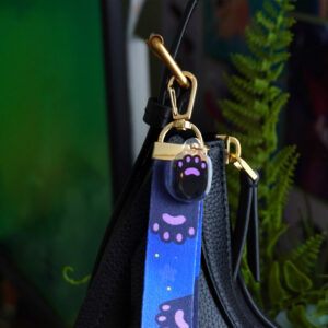 Purple lanyard with cat paw print & "meow" text design attached to a black handbag.