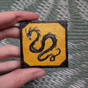 tiny square painting of a balck wyrm framed on shiny gold background