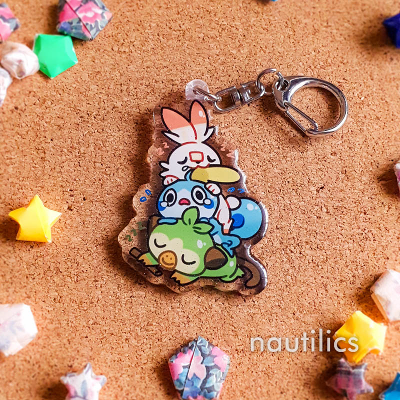 Pokemon Starters Acrylic Charms (B-Grade) by Nautilics Photo of an acrylic charm featuring the Galar Pokemon starters, stacked atop each other in a pile.