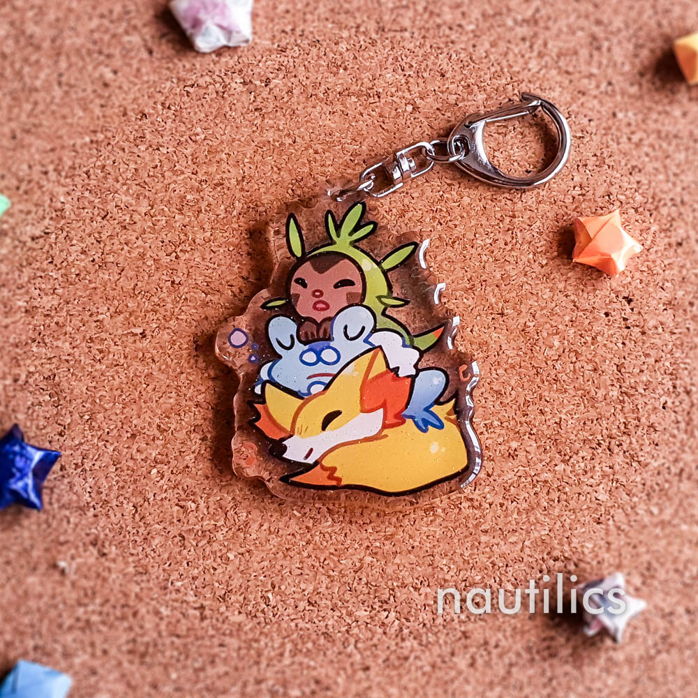 Pokemon Starters Acrylic Charms (B-Grade) by Nautilics Photo of an acrylic charm featuring the Kalos Pokemon starters, stacked atop each other in a pile.