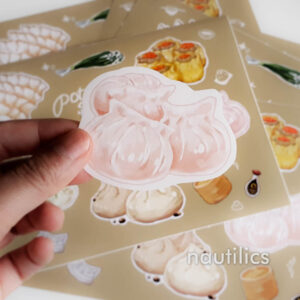 Photo showing an individual hargao sticker held up in front of the sheet of dumpling stickers.