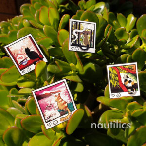 Photo of a set of four wooden pins featuring cats in polaroid-esque frames. The four cats are a black cat, orange tabby, calico cat, and a siamese cat. All cats have their backs to the viewer, and facing out on a different aesthetic scene.