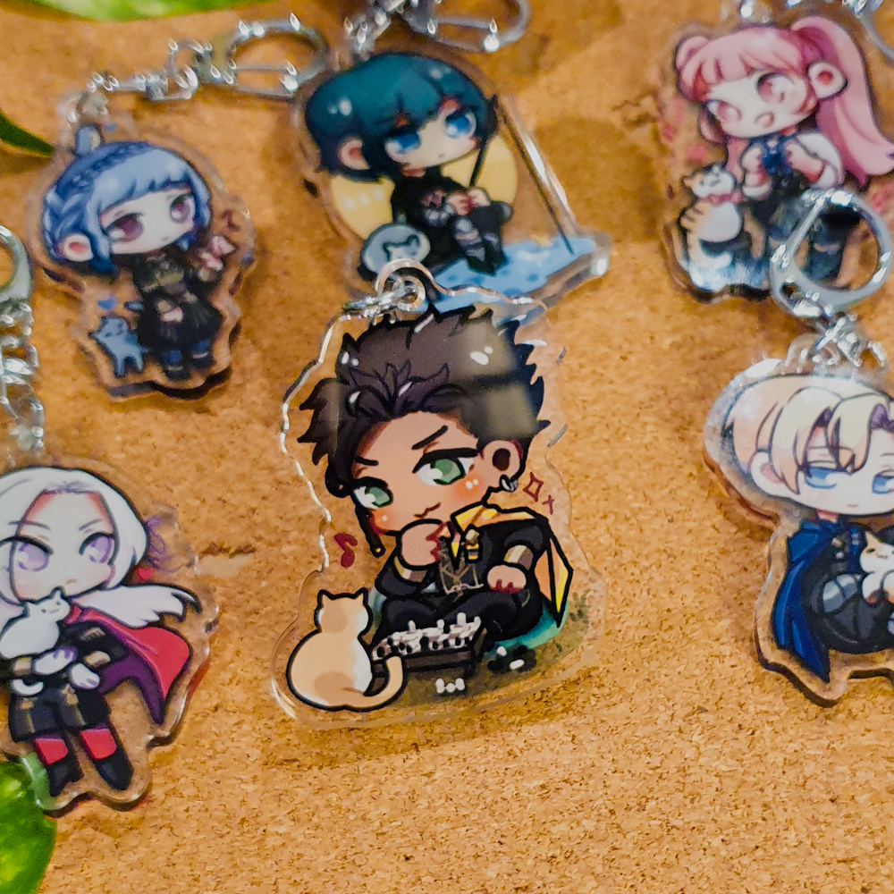 Fire Emblem: Three Houses Acrylic Charms by Nautilics Photo of acrylic charms of characters from Fire Emblem: Three Houses. The main focus of this photo is Claude playing chess with a cat, but other characters are visible in the background.