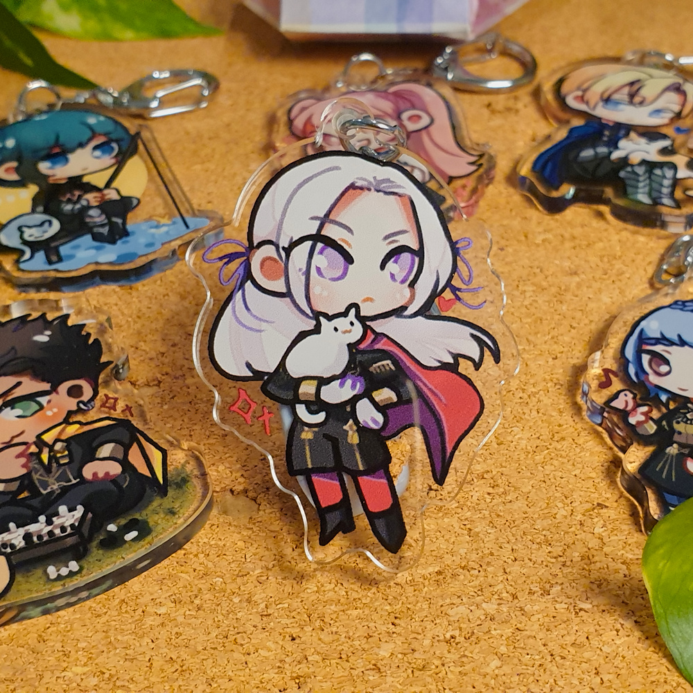 Fire Emblem: Three Houses Acrylic Charms by Nautilics Photo of acrylic charms of characters from Fire Emblem: Three Houses. The main focus of this photo is Edelgard majestically holding a small cat, but other characters are visible in the background.