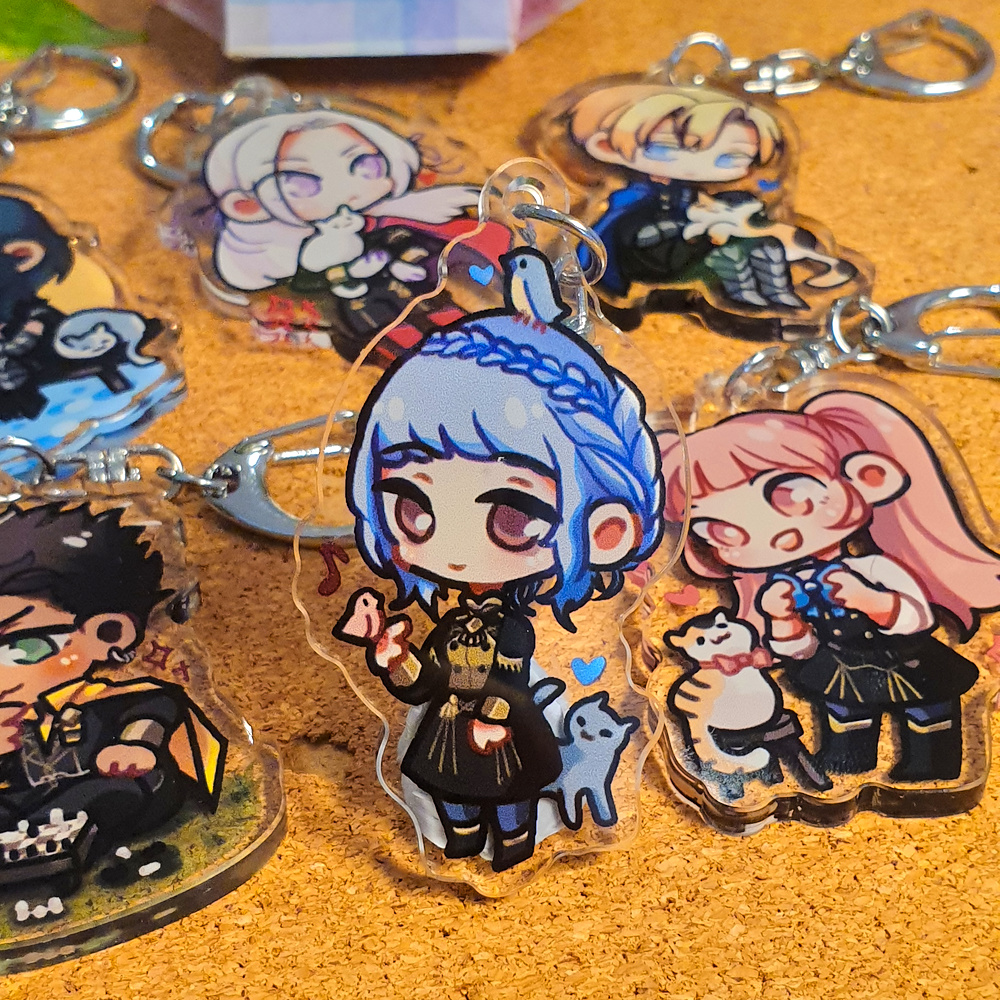 Fire Emblem: Three Houses Acrylic Charms by Nautilics Photo of acrylic charms of characters from Fire Emblem: Three Houses. The main focus of this photo is Marianne smiling gently at a bird and cat, but other characters are visible in the background.