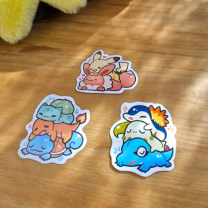 Photo of 3 pokemon stickers, with each one showing a stack of starter pokemon. The generations shown are starter pokemon from Kanto, Johto, and a stack with Pikachu and Eevee.