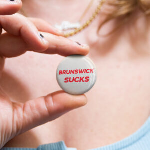 Australian badge saying “Brunswick Sucks" by Bordermind Baby – 32mm pin badge handmade in Melbourne