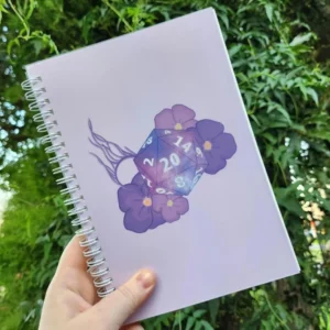 A5 spiral-bound hardback notebook featuring a Gale-inspired D20 design surrounded by refined, magical-themed floral artwork. The notebook includes 192 dot-grid pages.